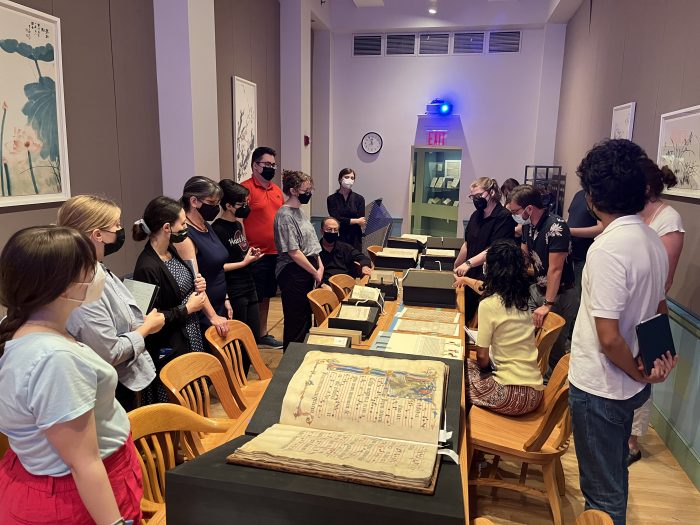 Students standing around a central table, lined with books open on special book displays, including an antiquated-looking music manuscript