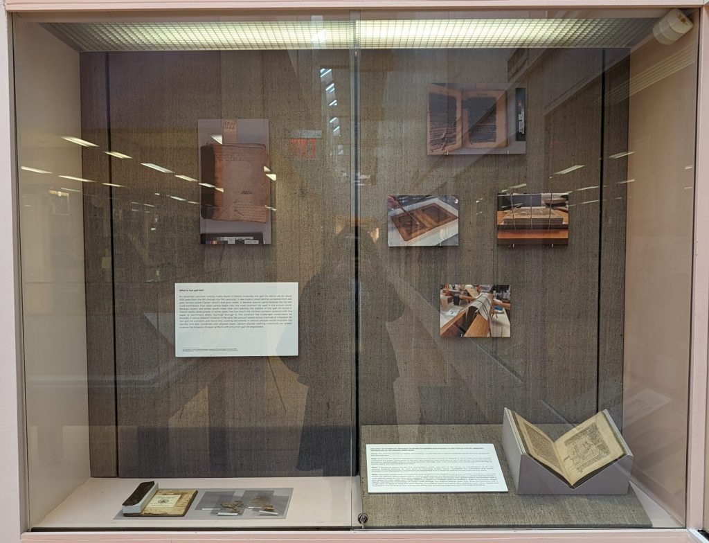 Image of an exhibition case featuring one manuscript, a (separated) binding, and images on the wall showing the conservation process.