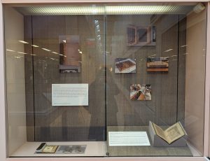 Exhibit case with a binding, extra manuscript fragments, and a manuscript on the bottom, and images showing various stages of the book's preservation on the wall. 
