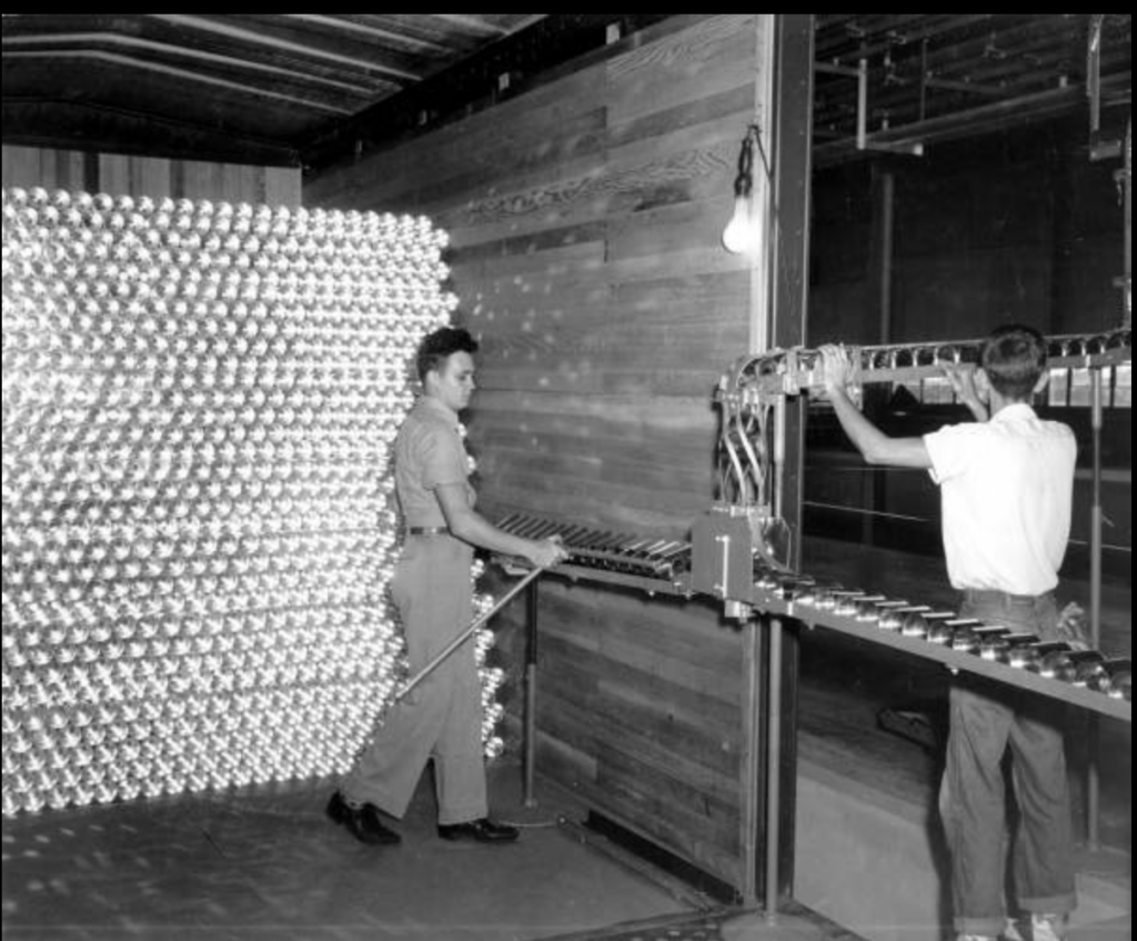 two whitem men in factory with wall of tin cans