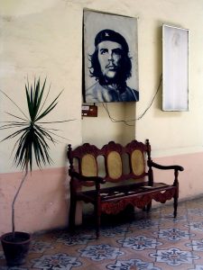 hallway painted in a cream color on top of wall and rose color on bottom with potted palm plant, a photo of Che Guevara hangs on the wall above a varnished wooden bench with wicker inlays